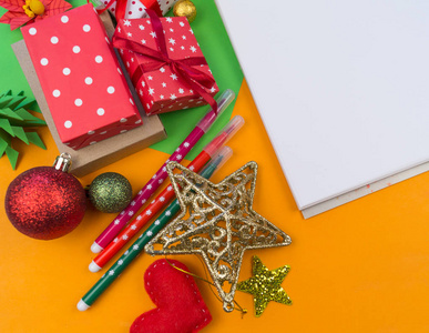 圣诞节装饰的装饰在橙色的背景上。 白色记事本写列表。 礼品包装材料。 历法。