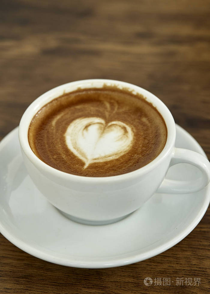 一杯带有心形图案的咖啡,放在白色的杯子里,背景是乡村木制的,有着