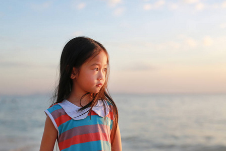 宁静的小女孩站在海滩上，在夕阳的灯光下眺望。