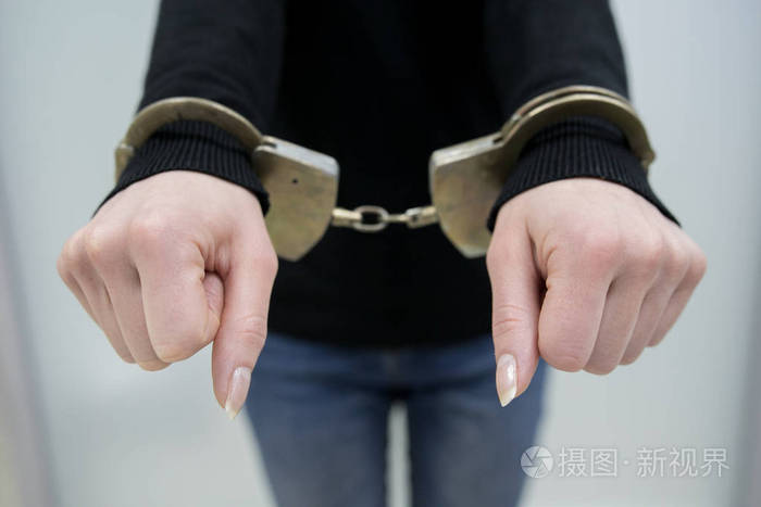 被逮捕的人用手铐将双手铐在灰色背景上背部.囚犯或被逮捕的手被铐.