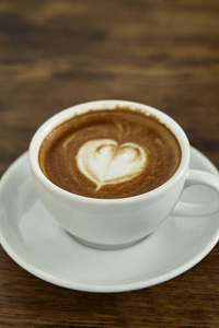 一杯带有心形图案的咖啡，放在白色的杯子里，背景是乡村木制的，有着美丽的拿铁艺术
