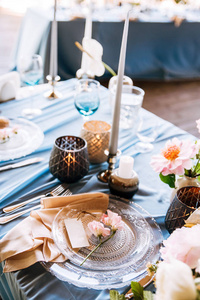 节日桌上有天蓝色的桌布，上面装饰着蜡烛和鲜花酒杯和刀叉
