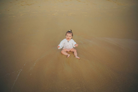 穿着白色衣服的小女孩在海浪中沙滩上玩沙子