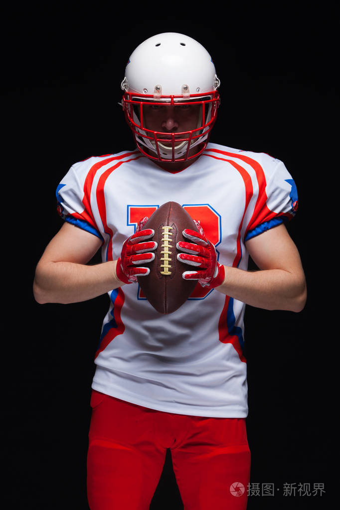 美国足球运动员戴着头盔在黑色背景下在他面前持球