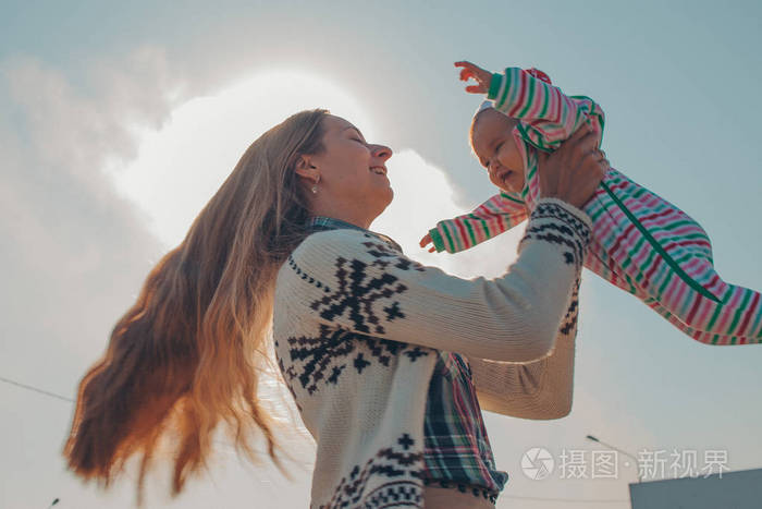 一个长头发的女人穿着针织毛衣,抱着一个穿着彩色条纹西装的小孩,对着