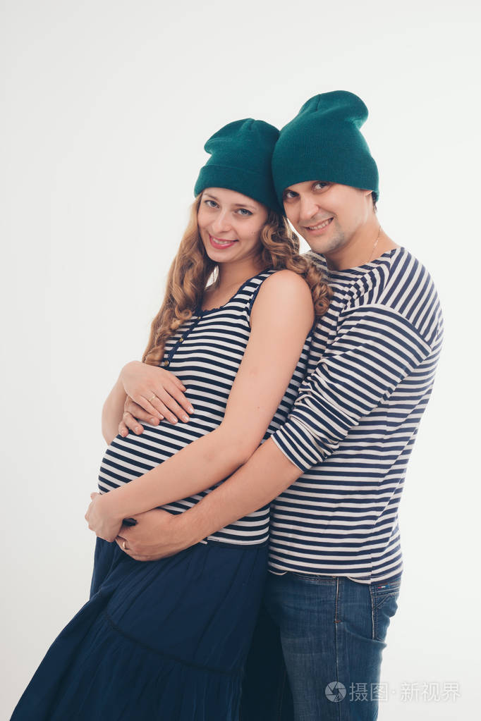 家庭肖像丈夫在白色背景上拥抱怀孕的妻子一男一女穿背心和帽子怀孕的