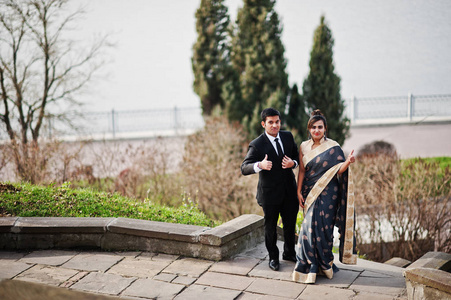 优雅时尚的印度朋友，一对穿着萨雷的女人和穿西装的男人在靠湖的楼梯上摆好姿势。