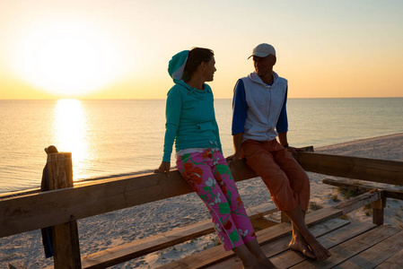 浪漫的夫妇在平房的阳台上放松，欣赏海上的日落，享受生活。 去海边的旅行太棒了。 背光。