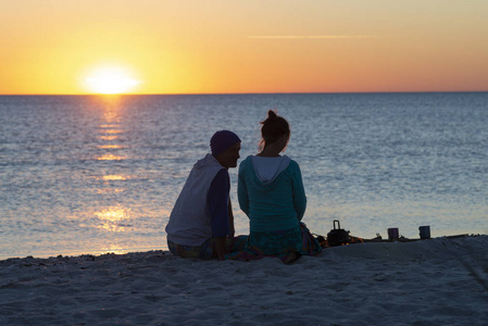 浪漫的夫妇在海滩上放松，喝咖啡，享受生活，欣赏海上的日落。 去海边的旅行太棒了。 背光背面视图。