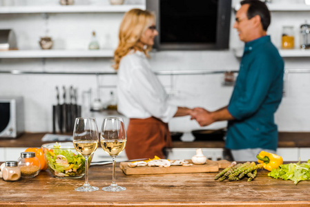 成熟的妻子和丈夫有选择地把注意力集中在厨房的蔬菜和桌面上的酒杯上