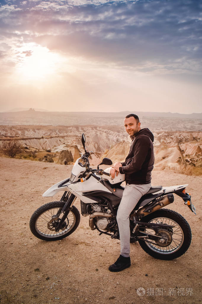 日落时英俊的男子骑着enduro摩托车骑着卡帕多西亚山脉山谷景观去