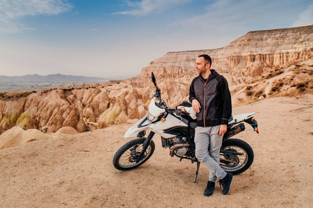 日落时，英俊的男子骑着Enduro摩托车骑着卡帕多西亚山脉山谷景观。 去土耳其旅游