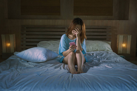 年轻抑郁的亚洲韩国女孩使用手机在床上哭泣，晚上感到悲伤和沮丧，网络欺凌或心碎的受害者，在绝望的女人的表情中抑郁