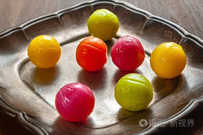 糖果球彩色悬垂硬水果糖果堆放在银碟木背景上
