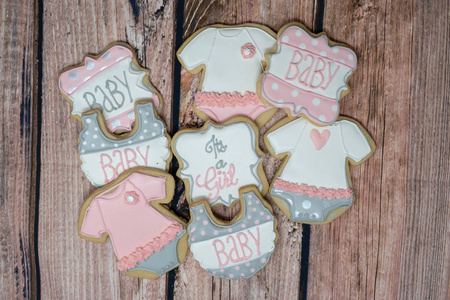 装饰的自制婴儿淋浴饼干，为女孩主题，装饰在粉红色灰色和白色的皇家糖霜在木制背景上。