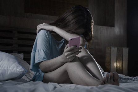 女性的绝望和悲伤年轻抑郁的亚裔中国女孩晚上用手机在床上哭泣,感到