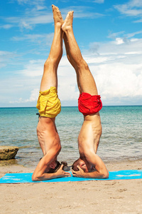 两个年轻人在海滩上一起做健身瑜伽运动。用于强度和平衡的 acroyoga 元素