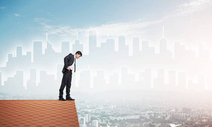 年轻的商人站在房子砖屋顶的边缘向下看混合媒体