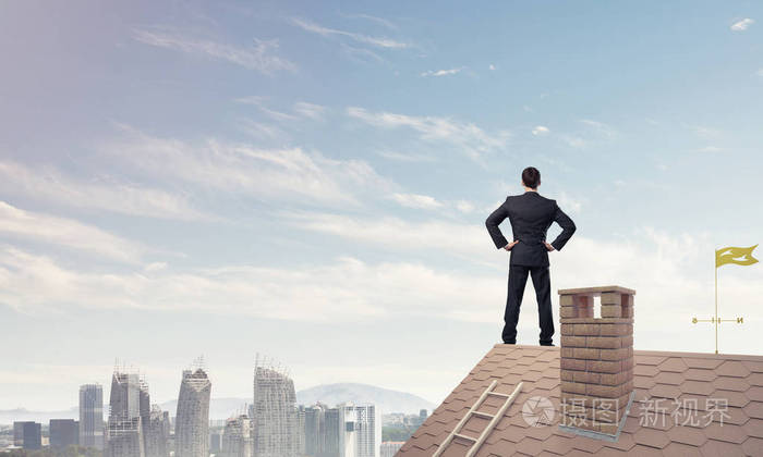 年轻坚定的商人站在屋顶上看着远方. 混合媒体