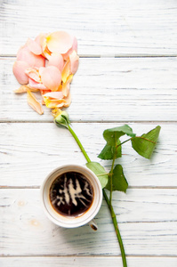 一杯咖啡，上面放着玫瑰花散落的花瓣，放在浅色的木制背景上