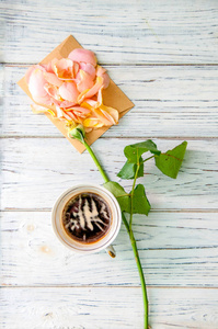 淡木色背景信封上有玫瑰花瓣的咖啡杯