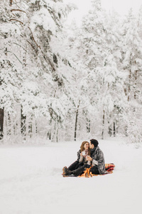 一对年轻夫妇在冬天的森林里约会，被火加热，喝可可