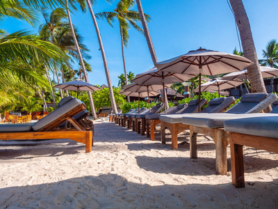海滩和海洋上的雨伞和椅子，蓝天环绕椰子棕榈树，供旅行和度假用