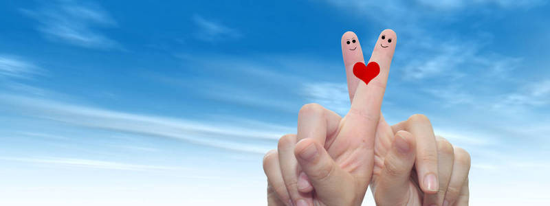 概念或概念人类或女性的双手，用两个手指画着红色的心和微笑的脸在云蓝色的天空背景横幅上