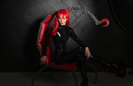 危险的残忍的恋物癖的红头发的女孩，穿着黑色的bdsm乳胶衣服，站在椅子上，穿着一种施虐受虐狂的风格。