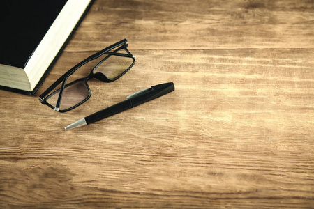 木制背景上的书眼镜和钢笔。
