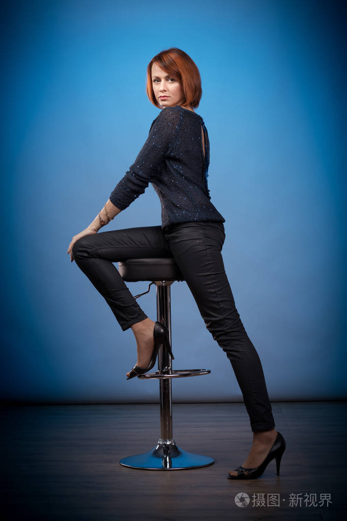 情绪激动的红发女人,穿着黑色衣服,坐在酒吧的凳子上,摆着蓝色的姿势