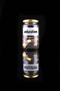 带有标签教育的瓶子中的硬币与黑色背景的金融概念隔离