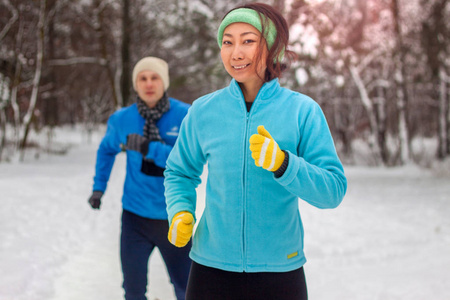 冬天，穿着运动服的年轻夫妇在公园里奔跑和微笑。一对夫妇在冬天的雪地里在新鲜空气中做运动。