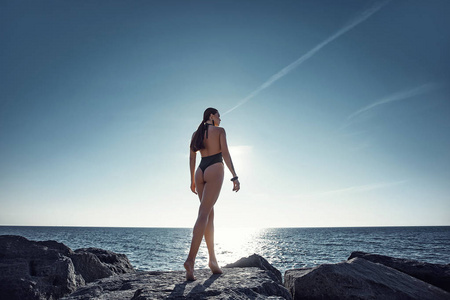 穿泳衣的漂亮女孩在海边的岩石上。后景。岛，日落，休息，晒太阳，旅游，自由..