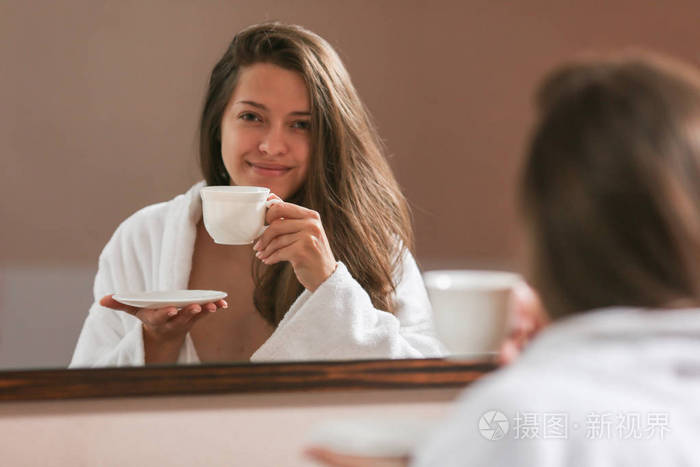 这位美丽的女人穿着浴袍，早上在酒店房间喝茶。