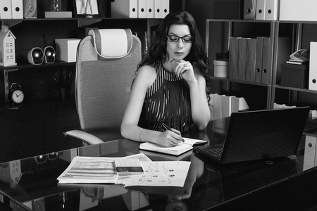年轻漂亮的商务女性，穿着时尚西装，戴着眼镜，在时尚的黑色电脑桌上工作。