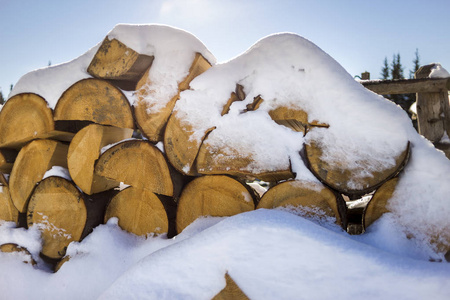 在明亮寒冷的冬天，阳光明媚的日子里，整齐地堆放着一堆切碎的干树干，木头覆盖着雪，背景火木原木准备过冬准备燃烧。