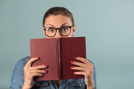 一个戴眼镜的年轻漂亮女孩拿着一本书，脸上带着惊讶的蓝色背景