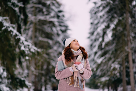 快乐的女性站在雪公园与一杯咖啡在手