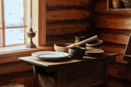 一个老农木木屋的内部碎片一张桌子，上面有木制和陶瓷盘子，还有煤油灯