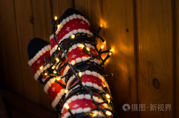 温暖的白色LED灯和脚在圣诞袜。 女孩在深夜在家放松。 寒假圣诞节和新年概念。