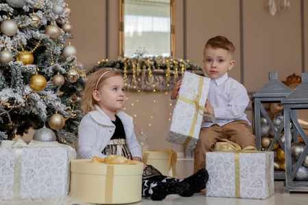 可爱的女孩和男孩打开圣诞礼物。 圣诞树下的孩子们带着礼品盒。 装饰客厅与传统消防场所。 温馨的冬天晚上在家。