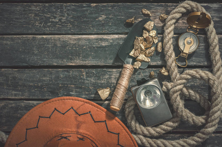 将金块放在铁锹绳子和老式手电筒上，放在老式的木桌背景上。 寻宝者或淘金者的概念。