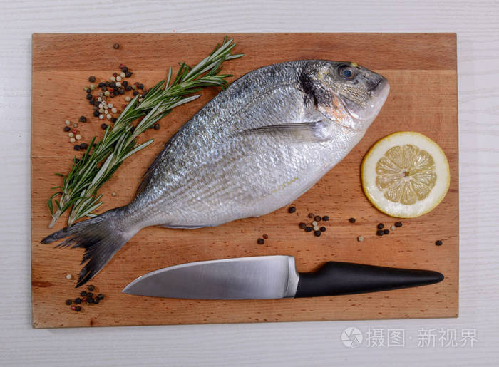 新鲜的多拉多鱼和迷迭香柠檬椒和小刀在木切割板上