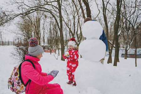 年轻的家庭男人，女人，穿着温暖的衣服，在雪地公园或户外森林里堆雪人。 假日的冬季乐趣休闲。 家庭生活方式观念