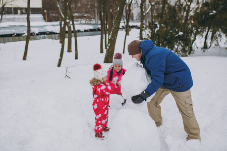年轻的家庭妇女，男人小女孩在冬天穿暖和的衣服玩耍，在雪地公园或森林户外堆雪人。冬季好玩，节假日休闲..家庭生活方式的概念