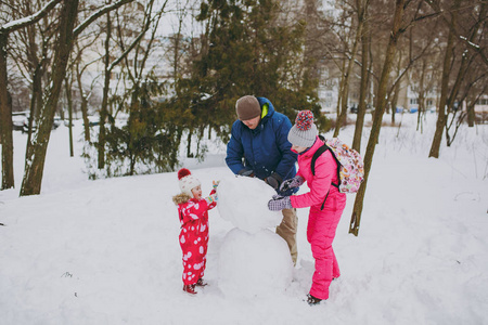 滑稽的家庭女人，男人小女孩在冬天温暖的衣服里玩耍，在雪地公园或森林户外堆雪人。冬季好玩，节假日休闲..家庭生活方式的概念
