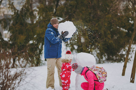 开朗的家庭女人，穿着温暖衣服的小女孩在玩雪人，男人在公园或森林户外拿着雪球。冬季好玩，节假日休闲..恋爱关系家庭生活方式