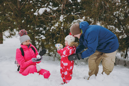 开朗的家庭女人，男人的小女孩在冬天保暖衣服玩耍，在雪地公园或森林户外做雪球。冬季好玩，节假日休闲..家庭生活方式的概念