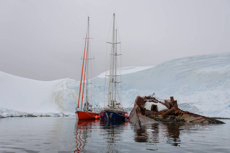 南极海域的两艘帆船停泊在生锈的沉船上